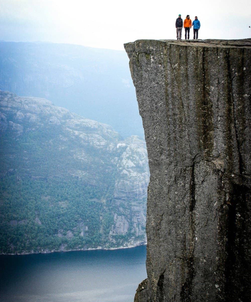 Tre turgåere står ytterst på Preikestolen over Lysefjorden